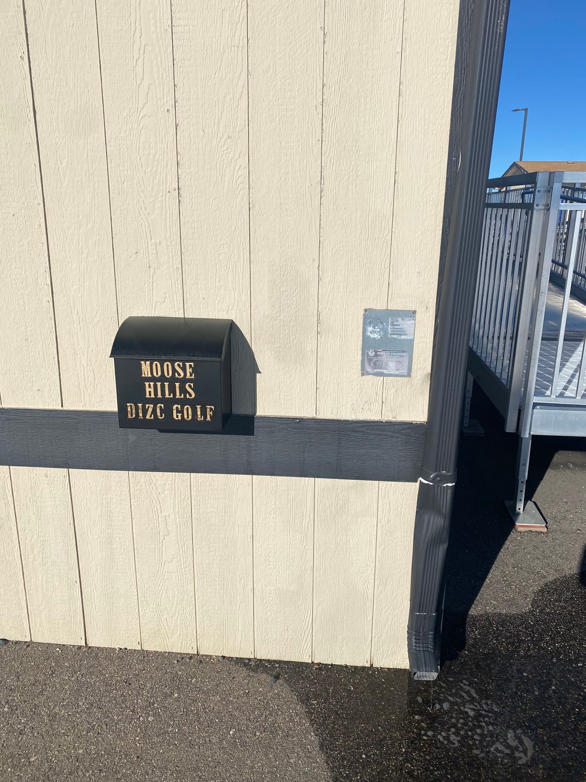 Disc drop box by the tee sign for hole 1 (back side of one of the preschool buildings)