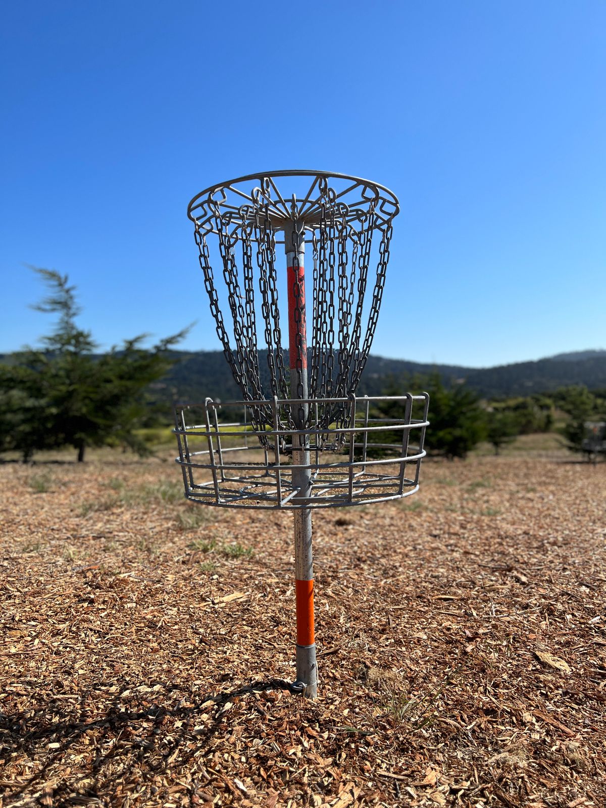 The practice putting area includes two baskets and is heavily carpeted with woodchips. It is wedged between the parking lot and the fairways of 19 and 27.