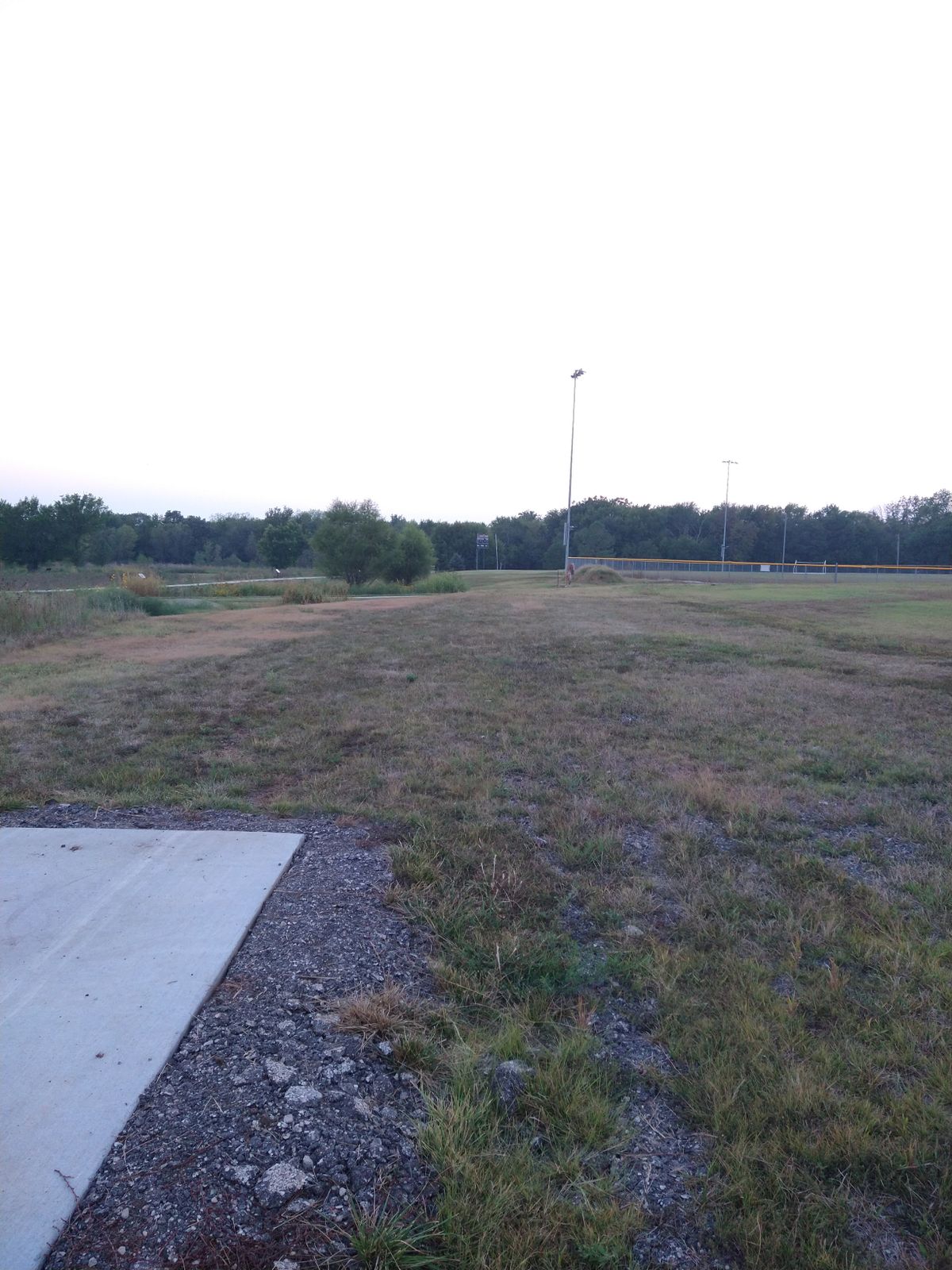 9th Tee is is near a softball field light pole. Plays straight west and over the fence or in the swamp are OB.