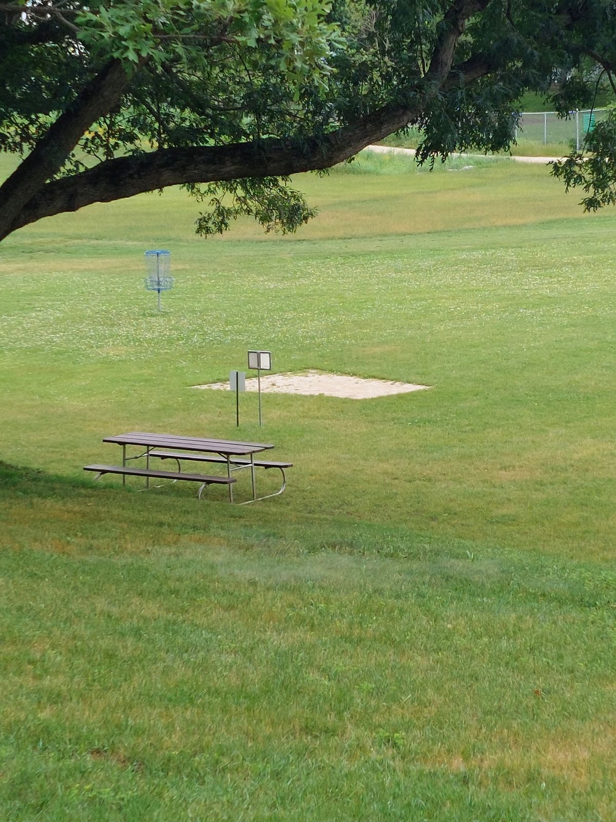 Hole #1 (taken from parking lot), practice basket in the background for a quick warm up. Only real defined tee pad (the others have signs)
