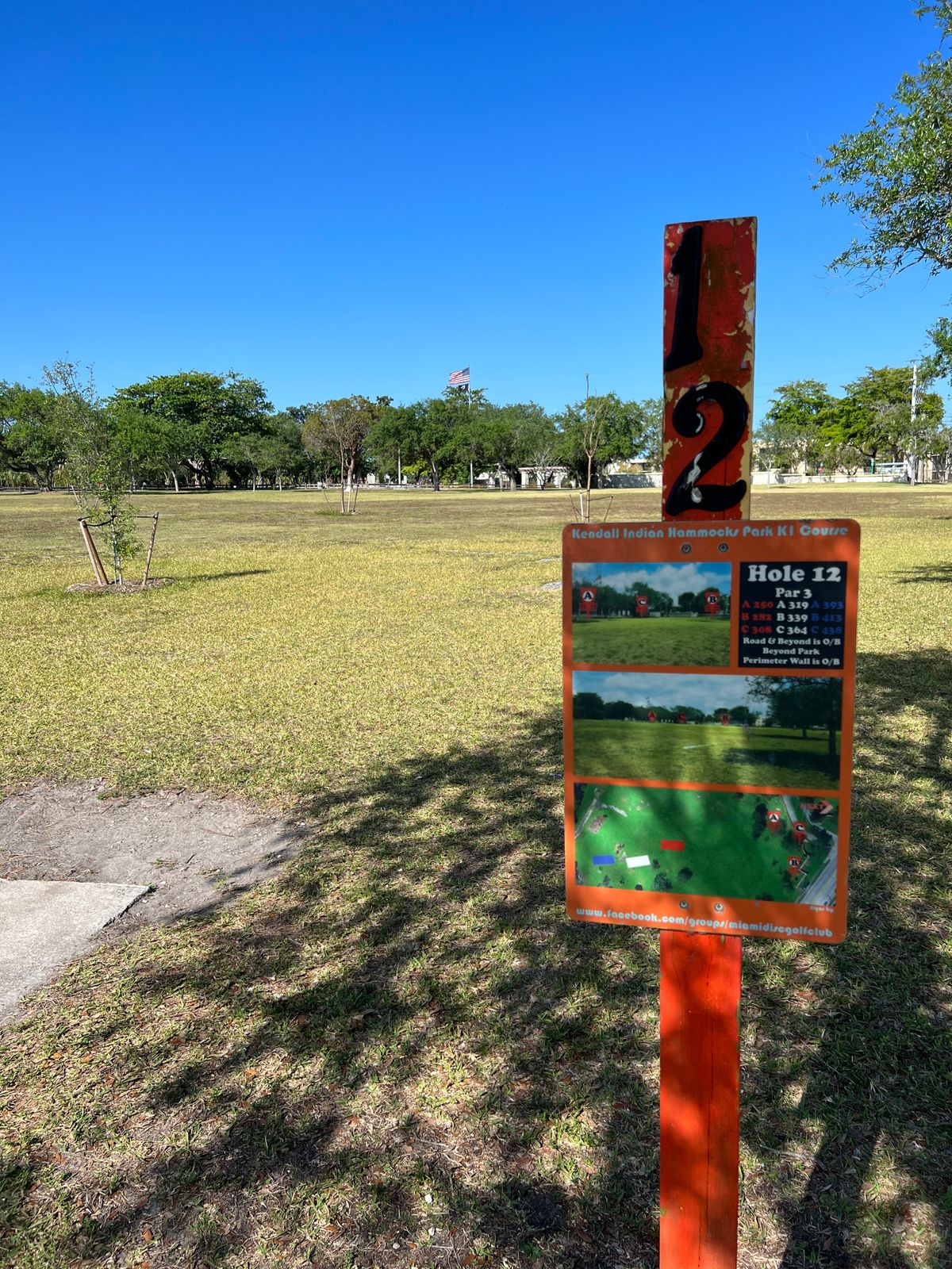 Hole 12 tee pad aim for American flag curve back to basket along wall by the street