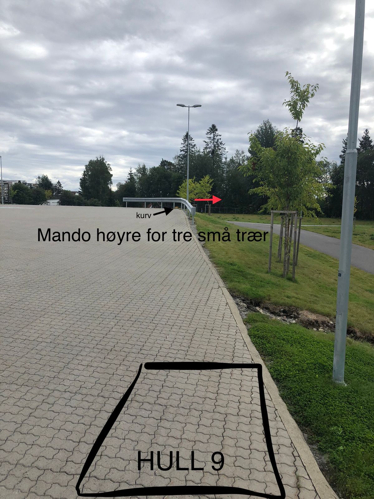 Hull 9. Mando til høyre for tre små trær langs grusveien. Ved bom dropzone til høyre for trærne.