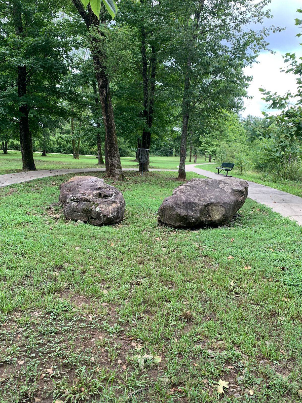 This hole 3 tucked back in trees & left sidewalk out. River on other side of right sidewalk