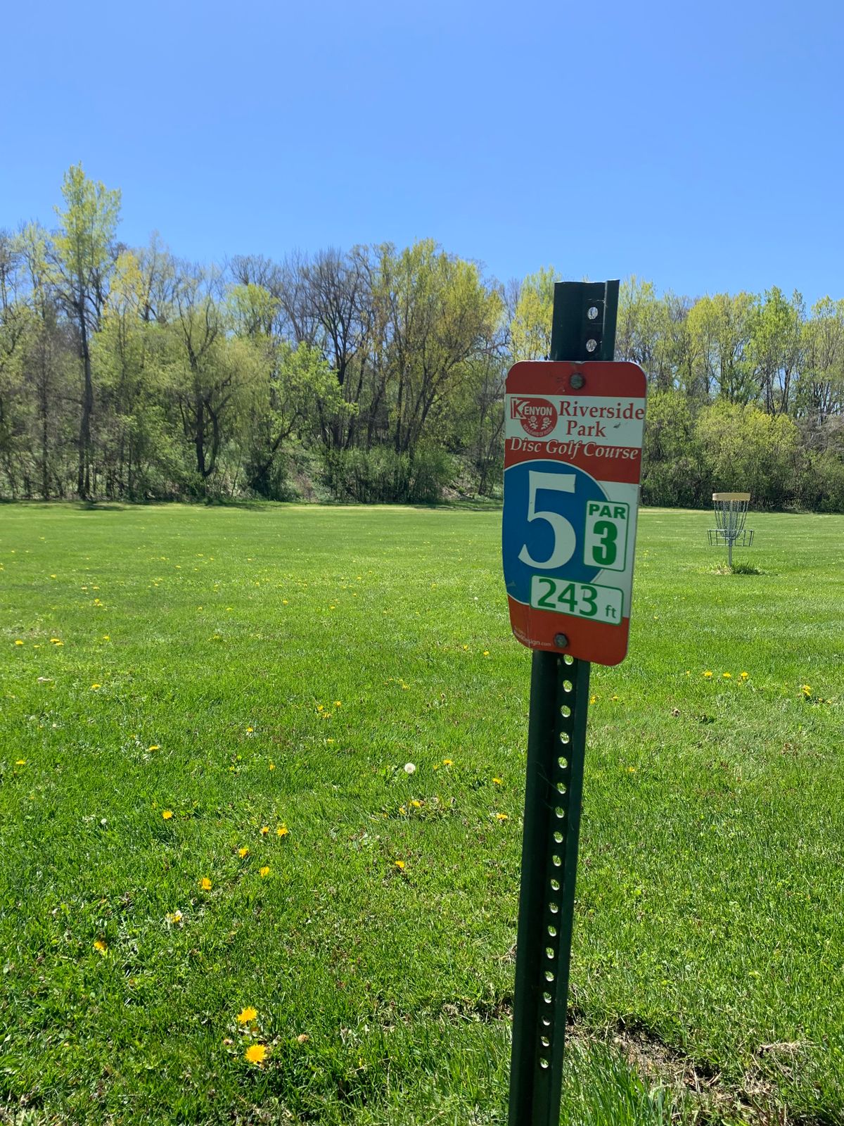 View of hole 5 tee sign. Basket tucked into a pocket of woods in the background.