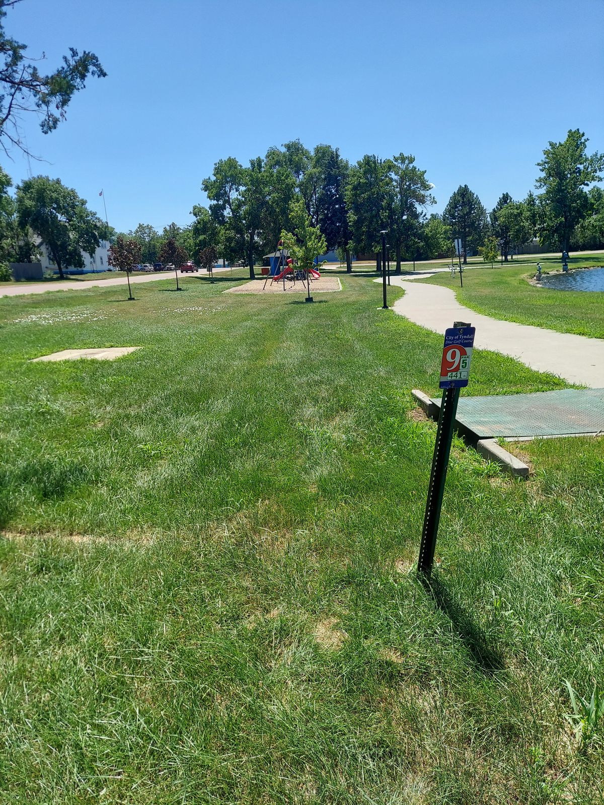 Backed up view teepad hole 9, playground directly in front of teepad. Hole is across the water and behind the bathroom