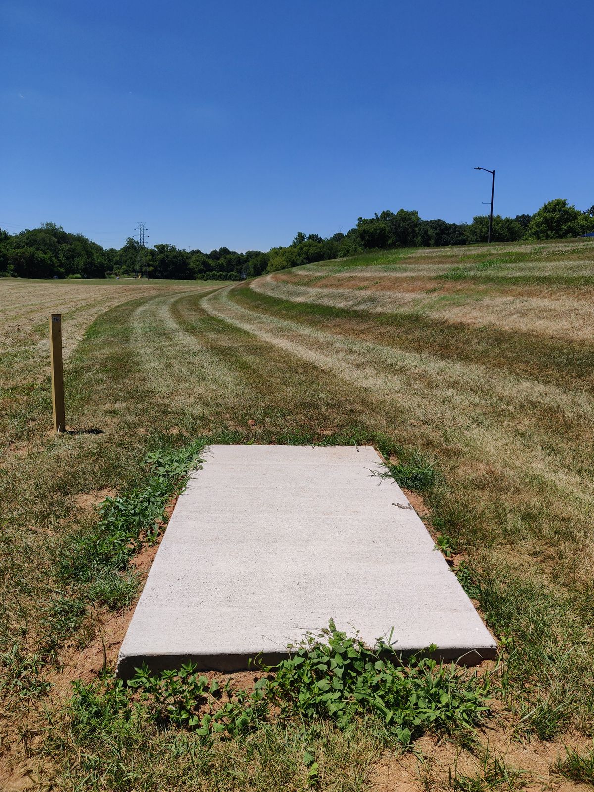 Hole 18. Looking down the fairway. Basket is centered with the tee pad behind the hill. Basket is raised half way up the hill. Road on the right plays as a hard OB.