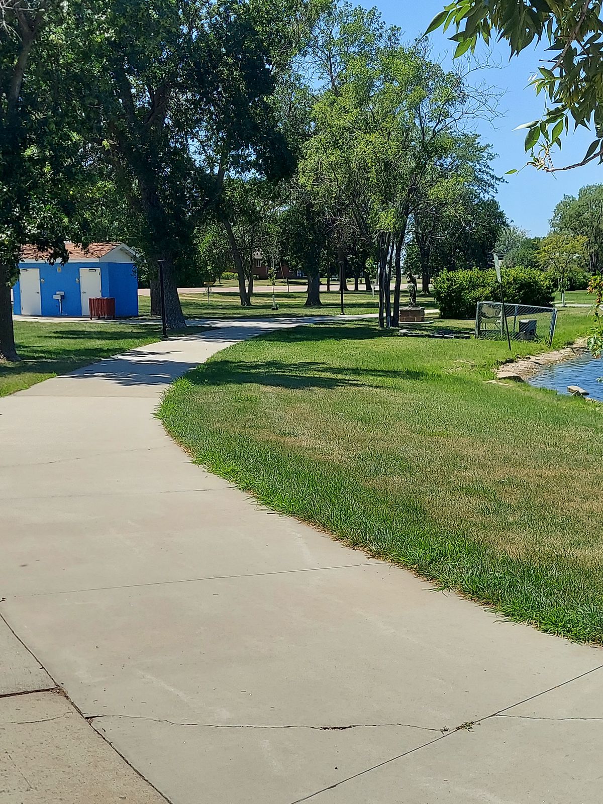 Thin landing area for hole 9, bathroom to the left. Trees, water, bushes to the right. Basket 9 is there in the background if you look close